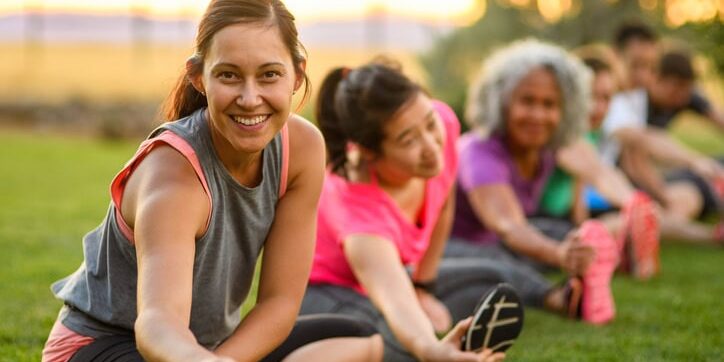 Woman stretching in group fitness class Portrait of a fit woman smiling directly at the camera while doing a seated leg stretch during a group fitness class outdoors in a public park on a beautiful summer evening in Oregon.
