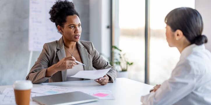Serious business woman, employer holding resume listening young candidate at job interview. Serious business woman, employer holding resume listening young candidate at job interview.