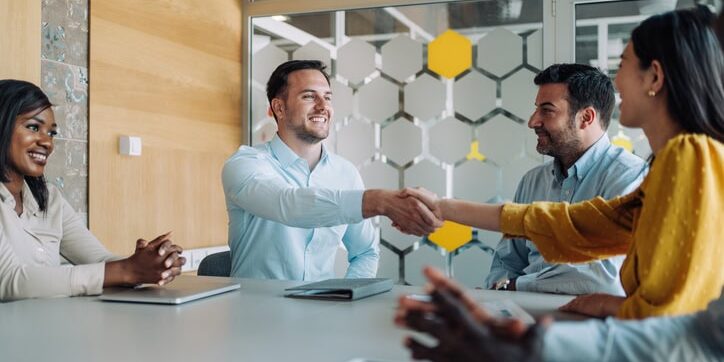 Businesswoman and businessman shaking hands across the table. Entrepreneurs handshaking during a meeting with their colleagues in the office. Business persons shaking hands on a meeting.