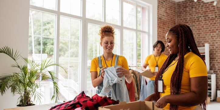 Diverse Young Women Sorting Clothing for Charity Diverse young women volunteers work side by side, sorting clothing donations in a charity center. The image captures the joy and sense of purpose that comes from helping others.